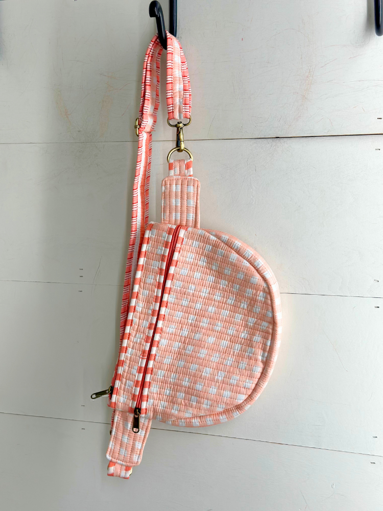 Pink checkered bag with a strap on a white wooden surface